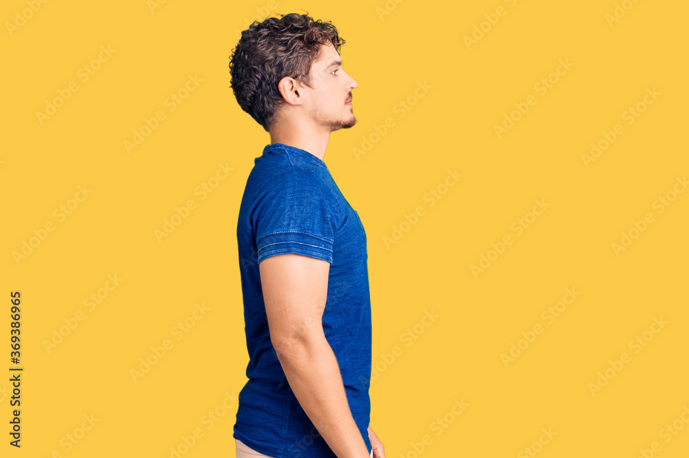 Young handsome man with curly hair wearing casual clothes looking to side, relax profile pose with natural face with confident smile.