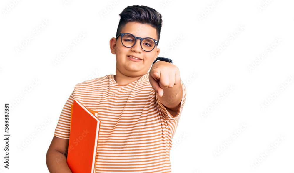 Little boy kid holding book wearing glasses pointing to you and the camera with fingers, smiling positive and cheerful Little boy kid holding book wearing glasses pointing to you and the camera with fingers, smiling positive and cheerful