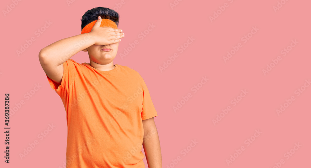 Little boy kid wearing sportswear covering eyes with hand, looking serious and sad. sightless, hiding and rejection concept