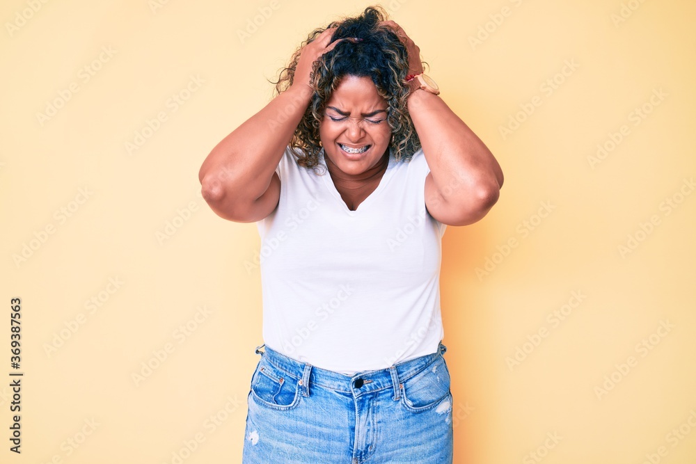 Young african american plus size woman wearing casual white tshirt suffering from headache desperate and stressed because pain and migraine. hands on head. Young african american plus size woman wearing casual white tshirt suffering from headache desperate and stressed because pain and migraine. hands on head.
