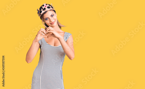 Young beautiful woman wearing king crown smiling in love showing heart symbol and shape with hands. romantic concept.