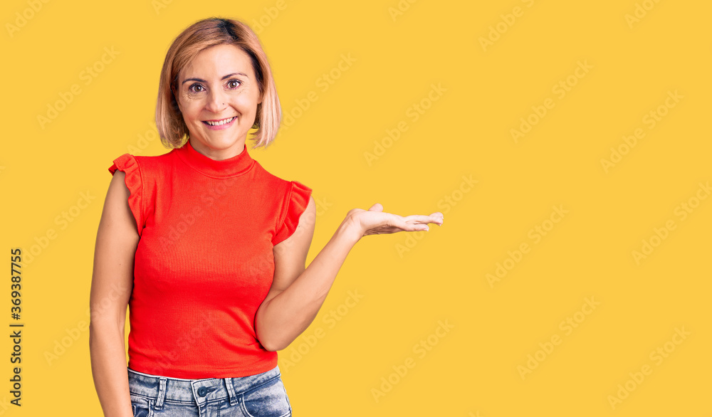 Young blonde woman wearing casual clothes smiling cheerful presenting and pointing with palm of hand looking at the camera. Young blonde woman wearing casual clothes smiling cheerful presenting and pointing with palm of hand looking at the camera.