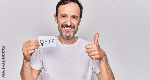 Middle age man asking for rights holding paper with equality male and female concept smiling happy and positive, thumb up doing excellent and approval sign