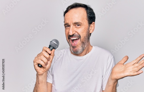 Middle age handsome singer man singing using microphone over isolated white background celebrating achievement with happy smile and winner expression with raised hand