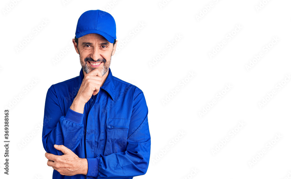 Middle age handsome man wearing mechanic uniform looking confident at the camera smiling with crossed arms and hand raised on chin. thinking positive. Middle age handsome man wearing mechanic uniform looking confident at the camera smiling with crossed arms and hand raised on chin. thinking positive.