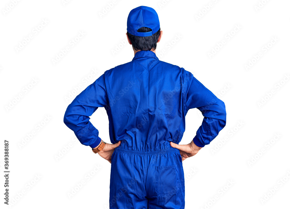 Middle age handsome man wearing mechanic uniform standing backwards looking away with arms on body Middle age handsome man wearing mechanic uniform standing backwards looking away with arms on body