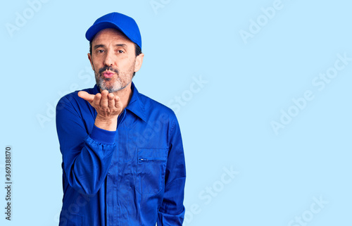 Middle age handsome man wearing mechanic uniform looking at the camera blowing a kiss with hand on air being lovely and sexy. love expression.