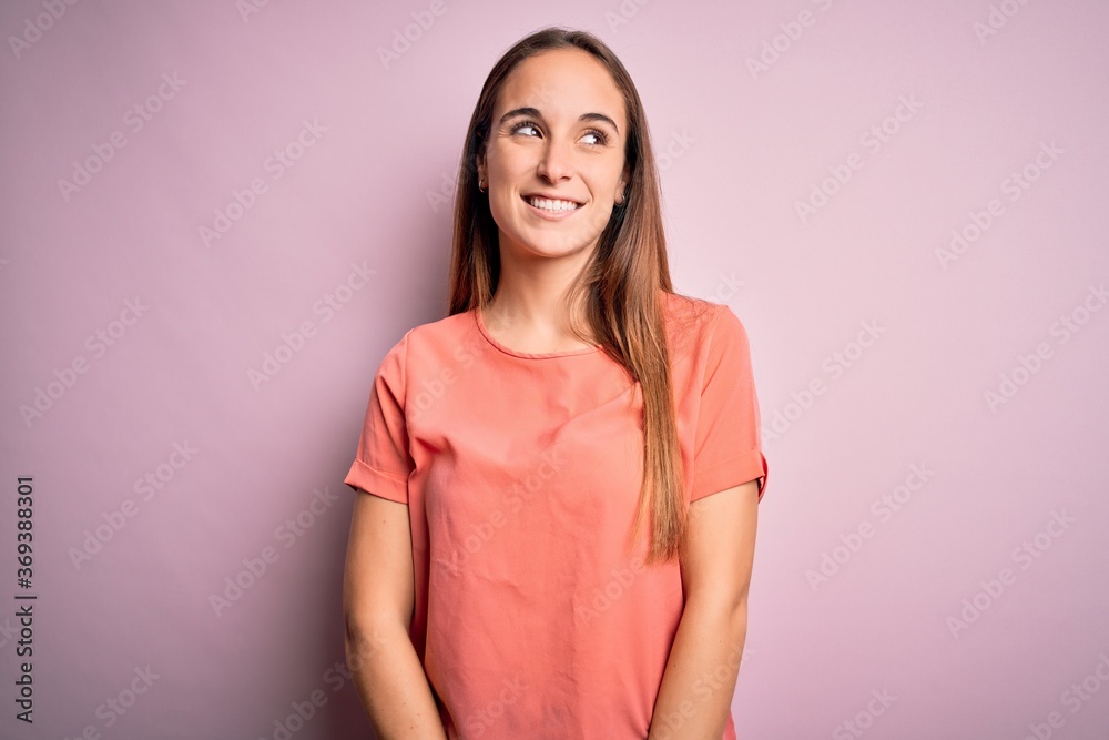 Young beautiful woman wearing casual t-shirt standing over isolated pink background looking away to side with smile on face, natural expression. Laughing confident. Young beautiful woman wearing casual t-shirt standing over isolated pink background looking away to side with smile on face, natural expression. Laughing confident.
