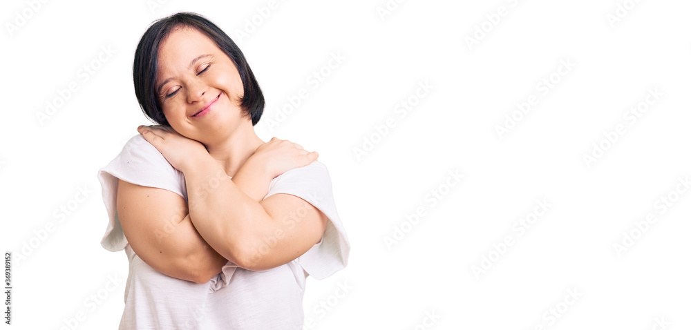 Brunette woman with down syndrome wearing casual white tshirt hugging oneself happy and positive, smiling confident. self love and self care Brunette woman with down syndrome wearing casual white tshirt hugging oneself happy and positive, smiling confident. self love and self care