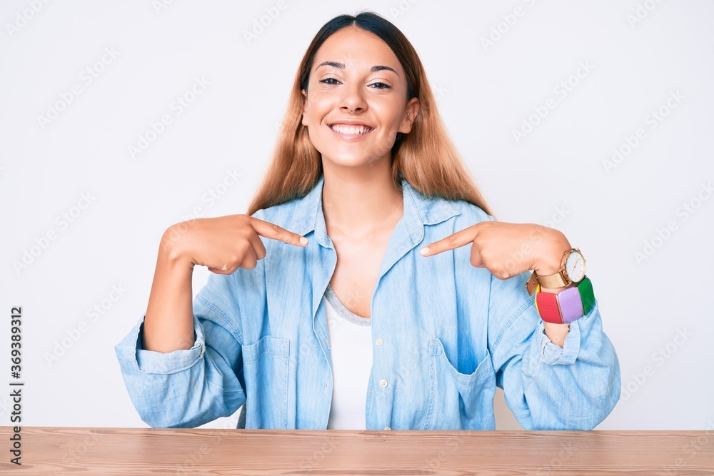 Young brunette woman sitting on the table wearing casual clothes looking confident with smile on face, pointing oneself with fingers proud and happy. Young brunette woman sitting on the table wearing casual clothes looking confident with smile on face, pointing oneself with fingers proud and happy.