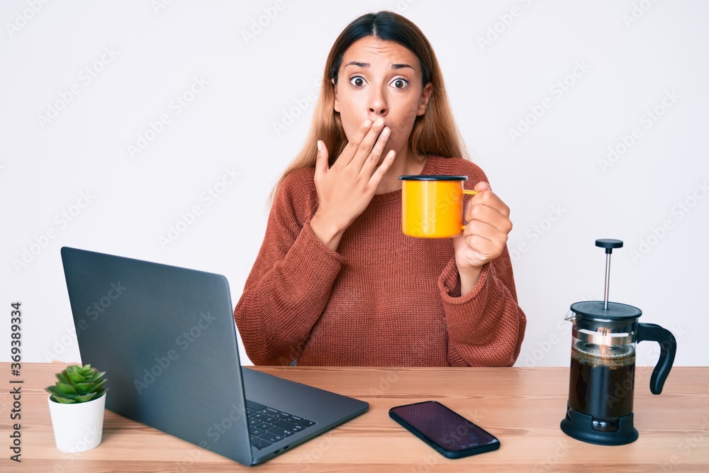 Young brunette woman working at the office drinking a cup of coffee covering mouth with hand, shocked and afraid for mistake. surprised expression Young brunette woman working at the office drinking a cup of coffee covering mouth with hand, shocked and afraid for mistake. surprised expression