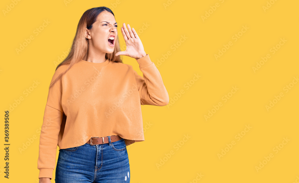 Beautiful young woman wearing casual clothes shouting and screaming loud to side with hand on mouth. communication concept. Beautiful young woman wearing casual clothes shouting and screaming loud to side with hand on mouth. communication concept.