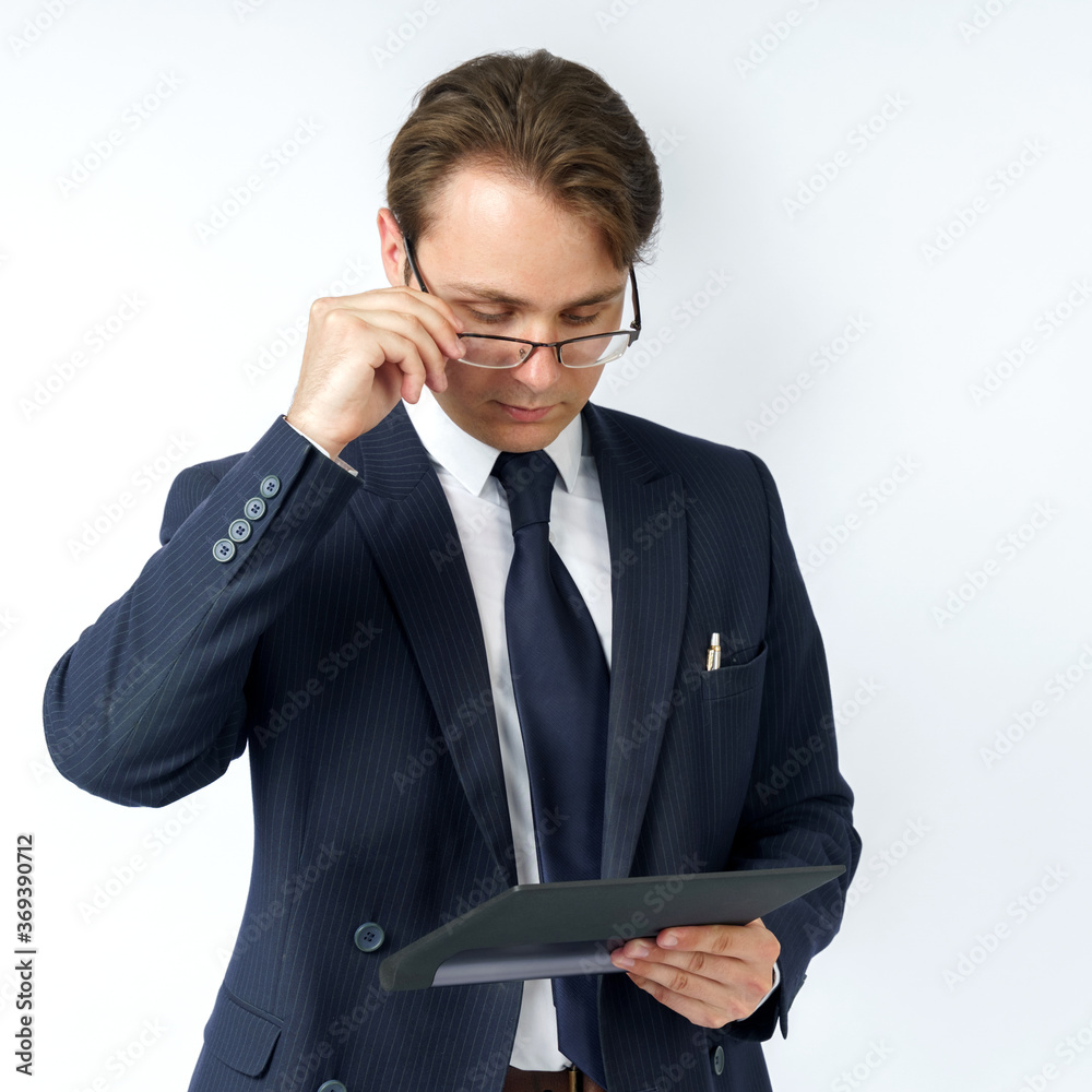 Portrait of a businessman in a blue suit who is holding an electronic tablet in his hands and adjusting his glasses. White background. Portrait of a businessman in a blue suit who is holding an electronic tablet in his hands and adjusting his glasses. White background.