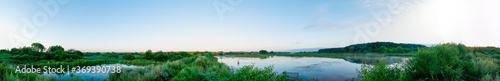Panoramic landscape from the lake with colorful clouds in the summer sun. © mikhailgrytsiv