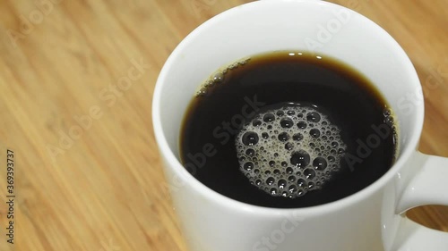 Top down slow motion coffee foame swirs in white cup on wood background.