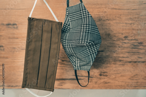 Stylish men face masks hanging in home closet. Different styles for fall outfits, brown fabric pleated and houndstooth plaid pattern mask. photo