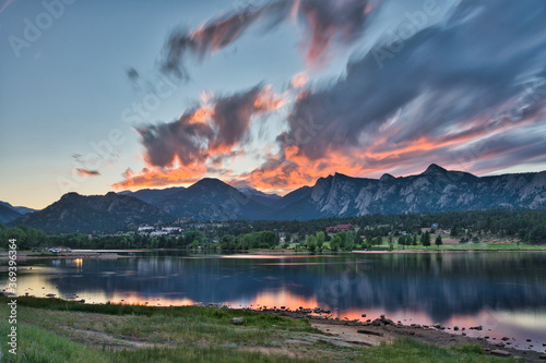 Long exposure sunset over lake estes. Fiery clouds roll over rocky mountains in the distance showing colorful reflection on the lake © Jordan