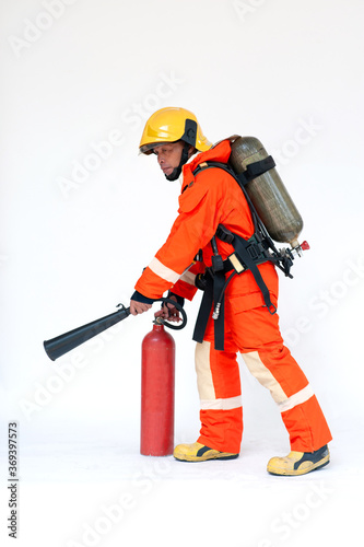 A portrait of Asian male firefighter in red protective uniform, mask and helmet with fire extinguisher standing on white background.