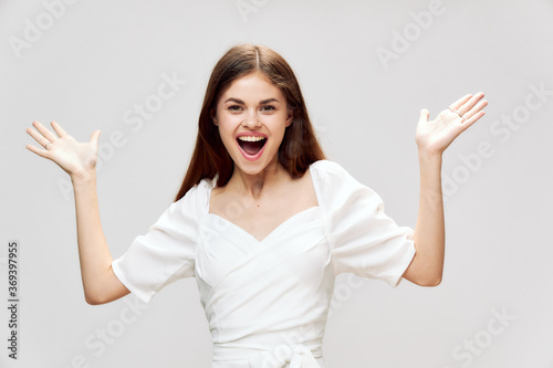 woman smiling broadly gesturing with hands white dress cropped view studio gray background