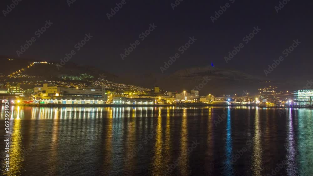 Stunning evening time lapse view from Laksevag looking toward Bergen center and Mount Ulriken. Scenic night view of colorful city lights reflected on smooth moving water of fjord in Norway. Stunning evening time lapse view from Laksevag looking toward Bergen center and Mount Ulriken. Scenic night view of colorful city lights reflected on smooth moving water of fjord in Norway.
