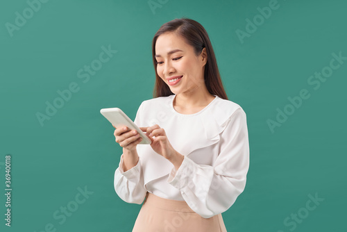 Smiling young woman girl using mobile phone typing sms message on turquoise background.