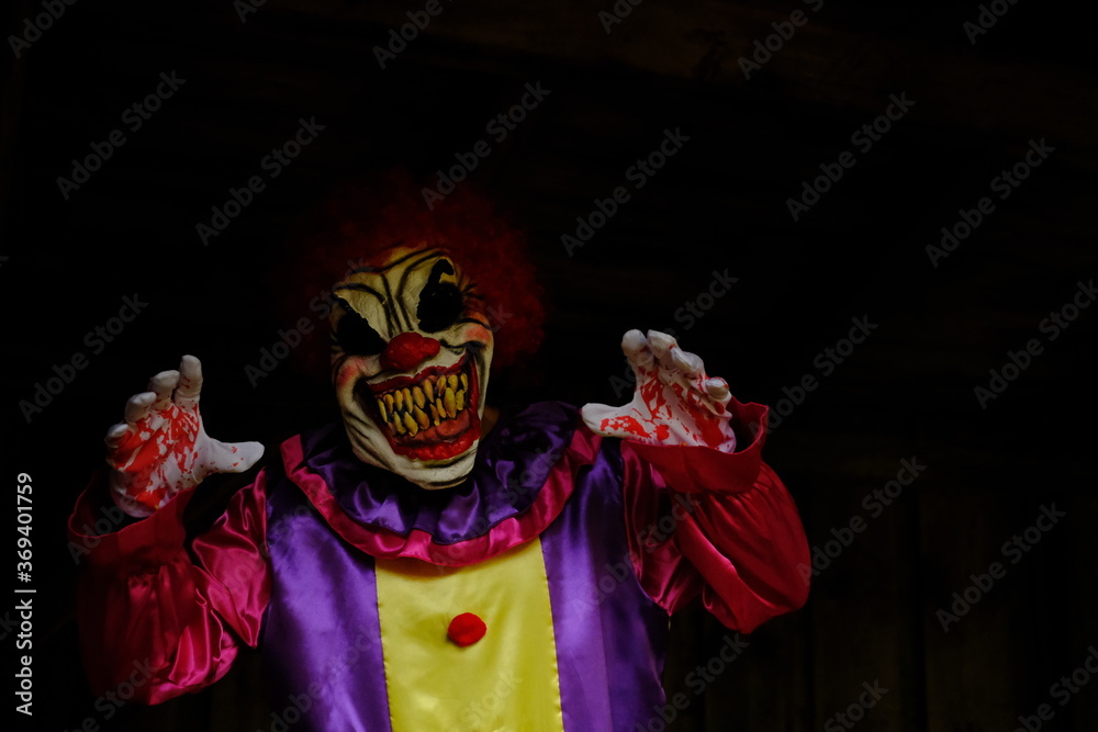 Halloween holiday. Creepy clown costume. Spooky clown in a  overalls  in a dark room.Autumn holidays in October. Festival and carnival concept. Horror and fear.Autumn seasonal holiday