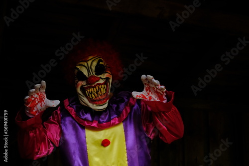 Halloween holiday. Creepy clown costume. Spooky clown in a overalls in a dark room.Autumn holidays in October. Festival and carnival concept. Horror and fear.Autumn seasonal holiday