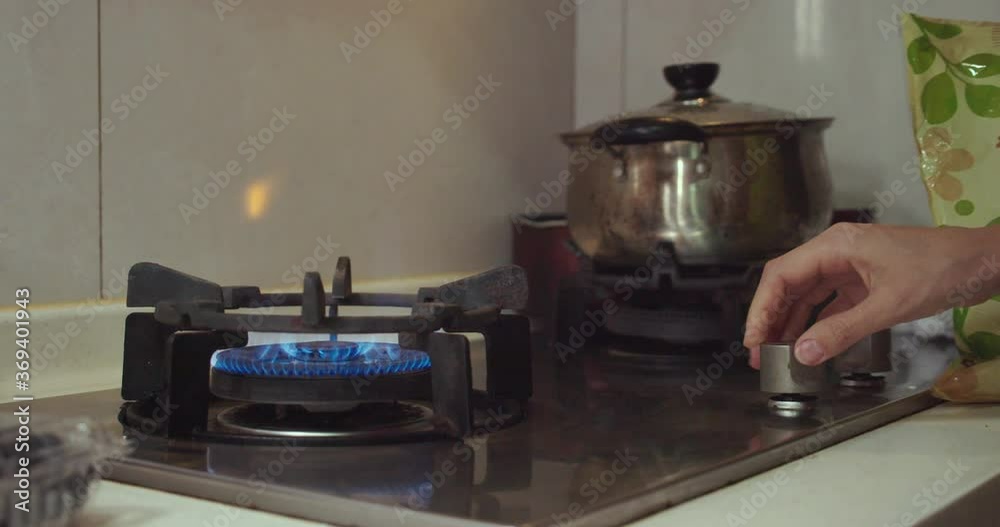 Woman hand turns switch on and ignites a gas cooking pan.