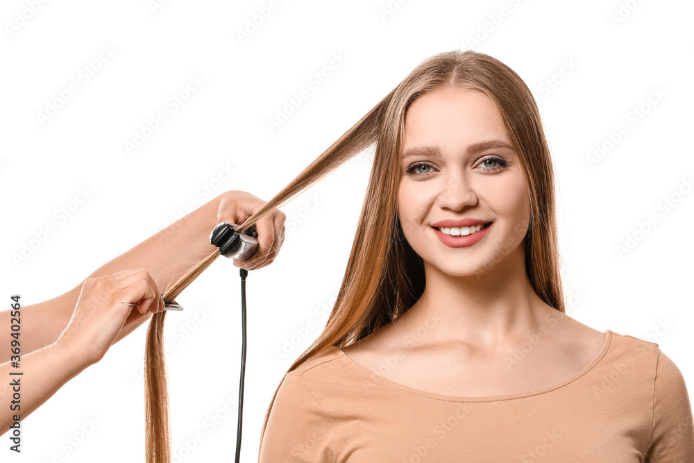 Hairdresser straightening hair of beautiful young woman against white background Hairdresser straightening hair of beautiful young woman against white background