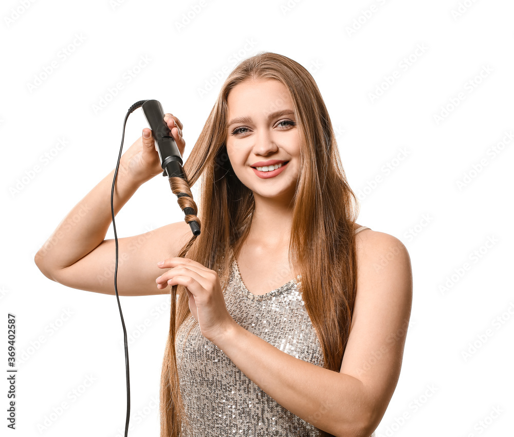 Beautiful young woman using curling iron for hair against white background