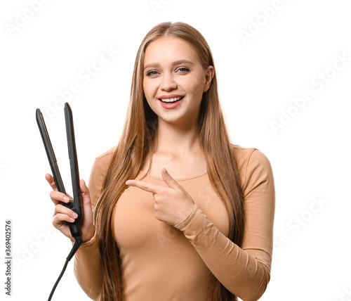 Beautiful young woman with flattening iron for hair against white background