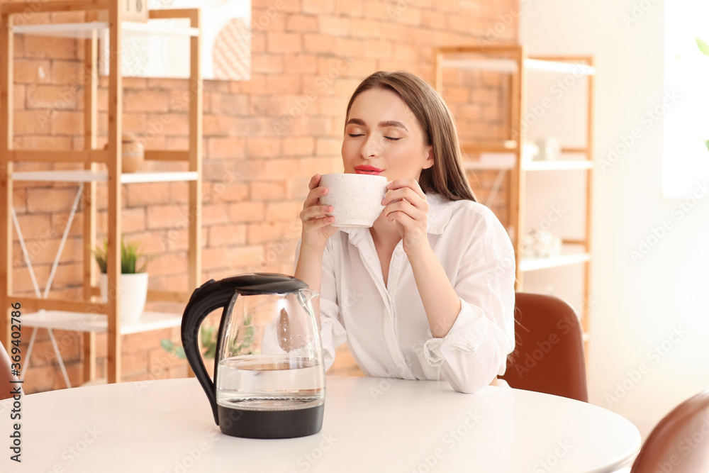 Woman with electric kettle drinking tea at home Woman with electric kettle drinking tea at home