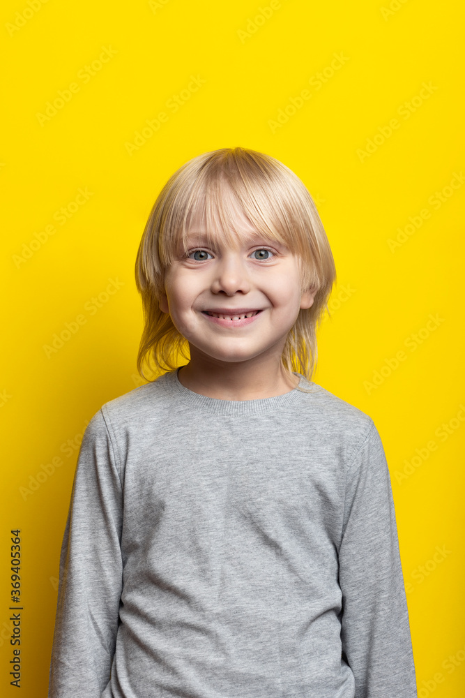 Portrait of cheerful fair-haired boy with long hair on bright yellow background. Vertical frame Portrait of cheerful fair-haired boy with long hair on bright yellow background. Vertical frame