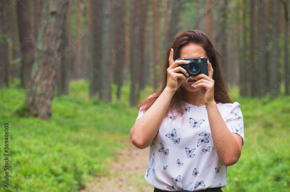 Cheerful girl takes pictures of the beauty of the forest with a retro camera