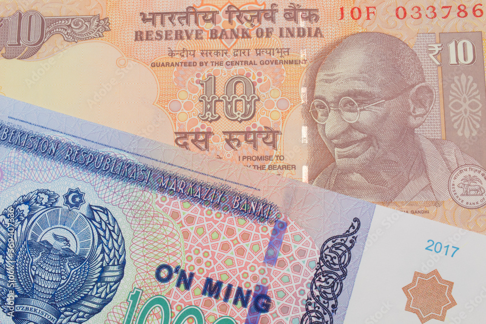 A macro image of a orange ten rupee bill from India paired up with a blue, white and green ten thousand som note from Uzbekistan.  Shot close up in macro.