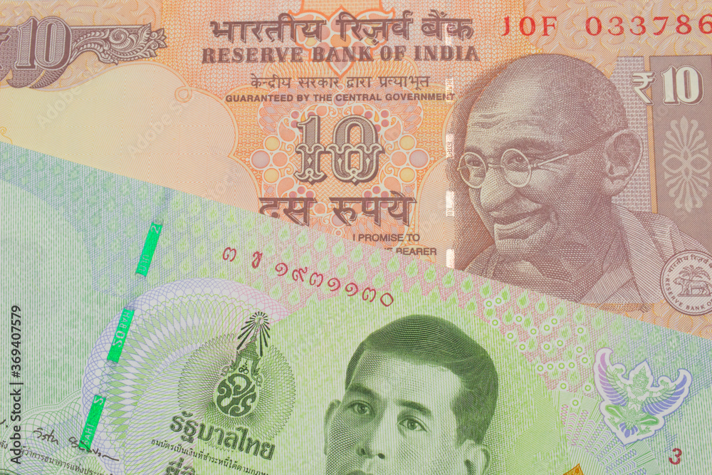 Fototapeta premium A macro image of a orange ten rupee bill from India paired up with a green twenty baht bank note from Thailand. Shot close up in macro.