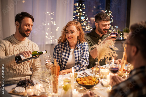 holidays and celebration concept - happy friends having christmas dinner at home pouring red wine