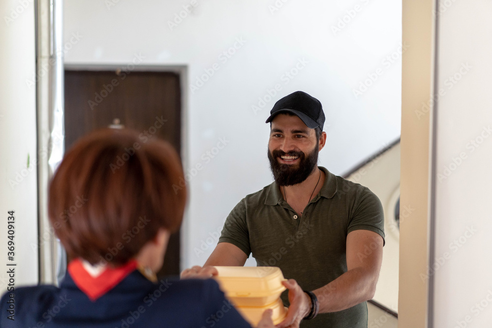 Delivery man with beard in green shirt carries food from restaurant to red hare middle age woman. Delivery man with beard in green shirt carries food from restaurant to red hare middle age woman.