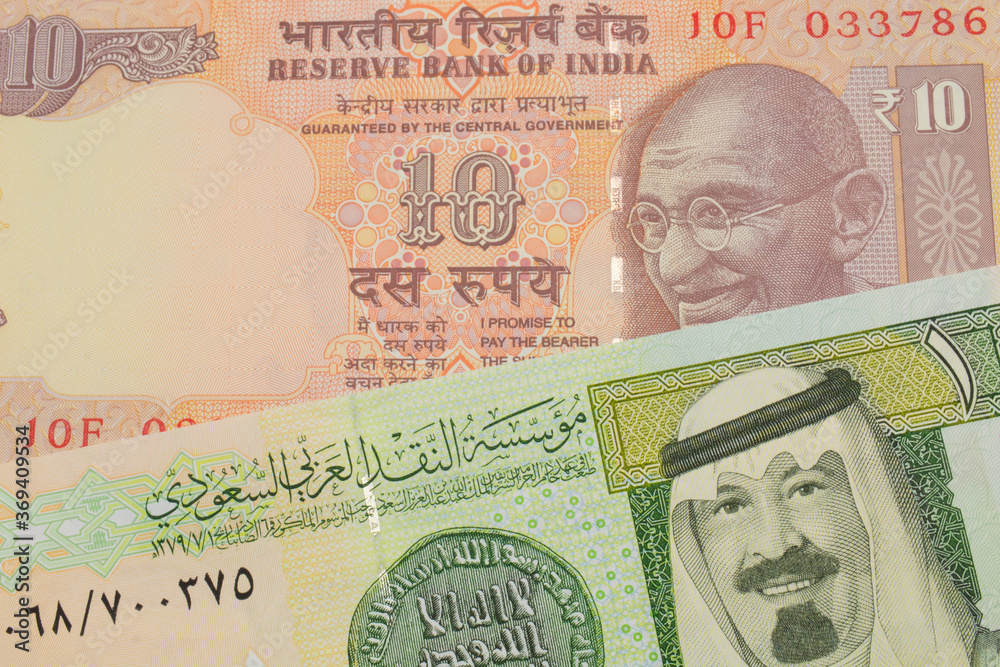 Fototapeta premium A macro image of a orange ten rupee bill from India paired up with a green and yellow one riyal bank note from Saudi Arabia. Shot close up in macro.