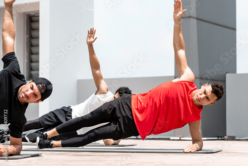 Handsome athletic men doing side plank bodyweight workout training outdoors on building rooftop in sunlight photo