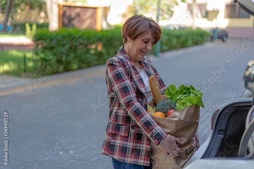 Carrying a healthy bag. Beautiful middle age woman holding paper bag full of fresh vegetables and smiling.  © Aleksandar