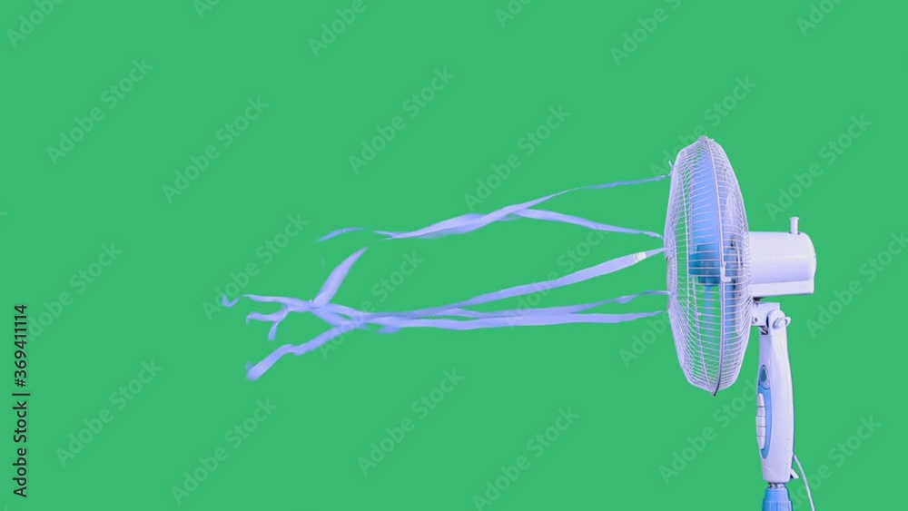 Side view of an electric fan with blue ribbons turning on,ventilating the space,eliminating the swelter,helping to avoid heatstroke.Studio shot on green background.Global warming,technology concept. Side view of an electric fan with blue ribbons turning on,ventilating the space,eliminating the swelter,helping to avoid heatstroke.Studio shot on green background.Global warming,technology concept.