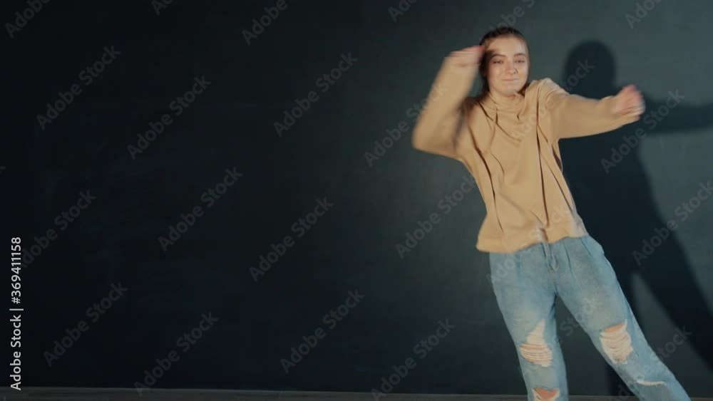 Pretty teen girl is dancing in dark studio performing beautiful creative dance alone having fun, performer is wearing trendy youth clothing. People and hobby concept. Pretty teen girl is dancing in dark studio performing beautiful creative dance alone having fun, performer is wearing trendy youth clothing. People and hobby concept.