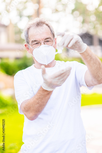 Senior man wearing protective mask applies an antibacterial antiseptic gel for hands disinfection and cleaning during flu virus outbreak, coronavirus epidemic and infecti photo