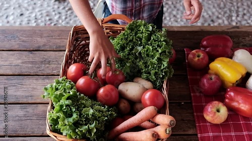 Young farmers who are learning the profession of farmer dressed as country men filling a wicker basket of fresh fruit and vegetables from the garden on a rustic wooden table of an agricultural farm
