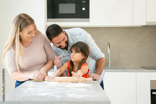 Joyful mom and dad staining girls face with flower while baking together. Young parents and daughter having fun while cooking in kitchen. Family home activity concept