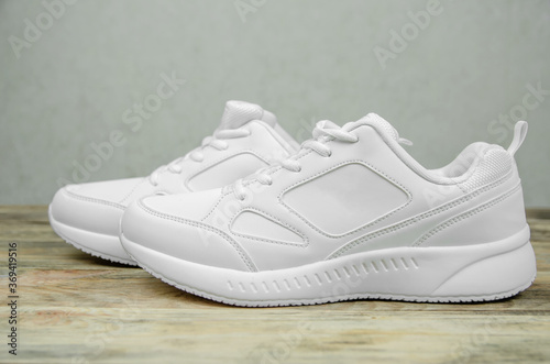 Beautiful pair of new white sneakers on a wooden background close up