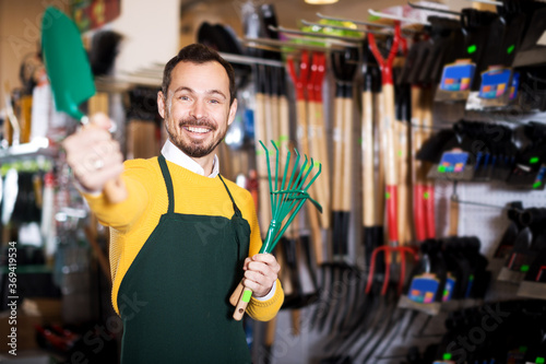 Glad young man seller displaying various items in garden equipment shop