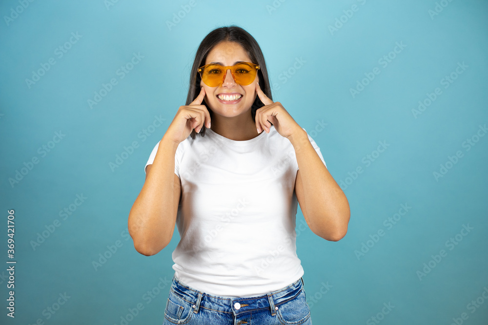 Young beautiful woman wearing sunglasses over isolated blue background smiling confident showing and pointing with fingers teeth and mouth