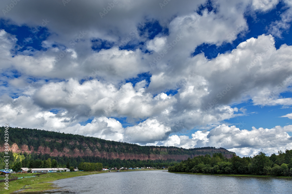 View of long cliff in Shamanka village in Russia wih blue sky and clouds background near river View of long cliff in Shamanka village in Russia wih blue sky and clouds background near river